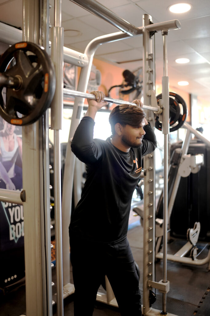 Man performing squats on Smith machine in gym, focused and wearing Curve Fitness Pro apparel.