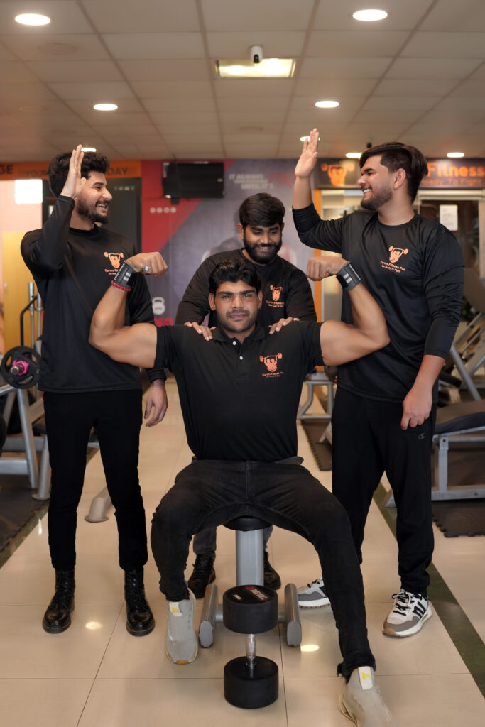 Four men in gym gear posing proudly, with one flexing muscles while others cheer him on.