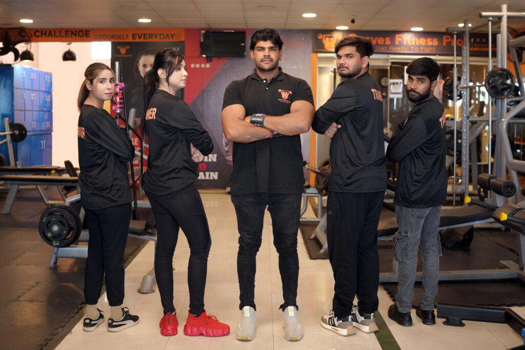 Curve Fitness Pro trainers posing confidently in the gym, wearing branded black uniforms and sneakers.