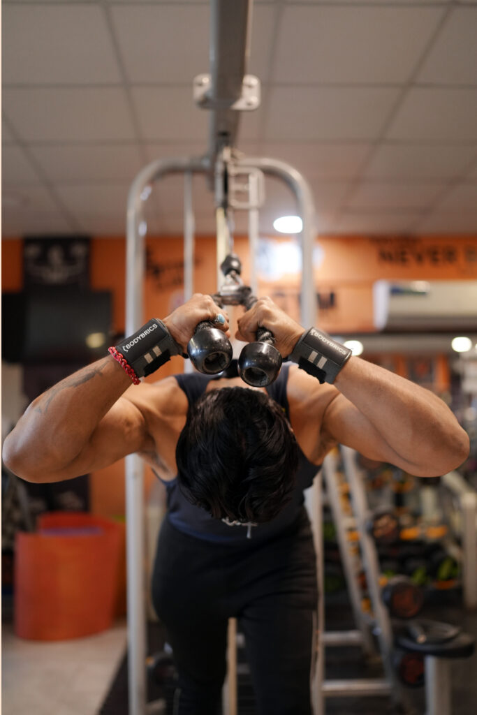 Man doing tricep pushdown with rope in gym, wearing Curve Fitness Pro wrist straps.