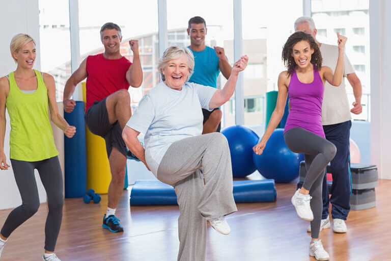 Group of older and younger adults smiling and exercising together in a bright fitness studio.